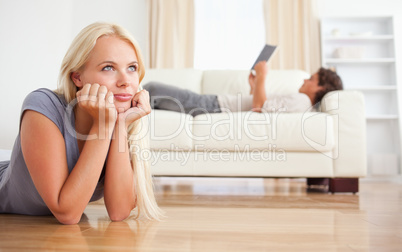 Woman lying on the floor while her fiance is reading a book