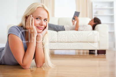 Woman lying on the floor while her husband is reading a book