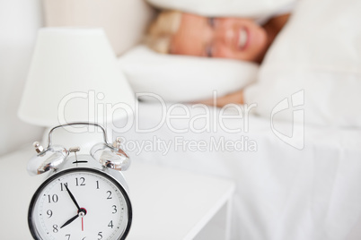 Woman hidding her head in a pillow while the alarrmclock is ring