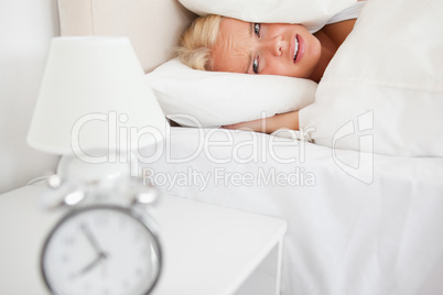 Tired woman hidding her head in a pillow while the alarmclock is