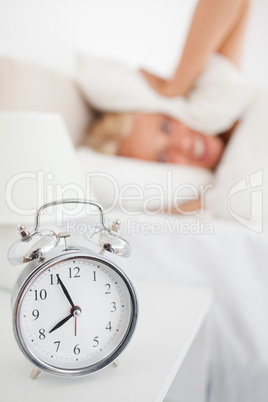 Portrait of a woman hidding her head in a pillow while the alarm
