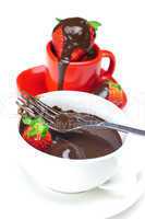 melted chocolate in a cup, fork and strawberries isolated on whi