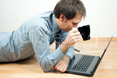 young man with cup using laptop  lying on the floor in the room