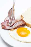 bacon with  fried  eggs on a plate, fork and bread isolated on w