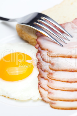 bacon with  fried  eggs on a plate, fork and bread isolated on w