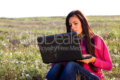 young beautiful woman with a laptop sitting in the field on sky