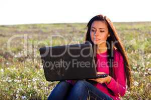 young beautiful woman with a laptop sitting in the field on sky