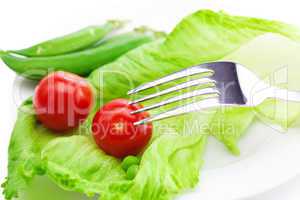 tomato,peas and lettuce with a fork on a plate isolated on white