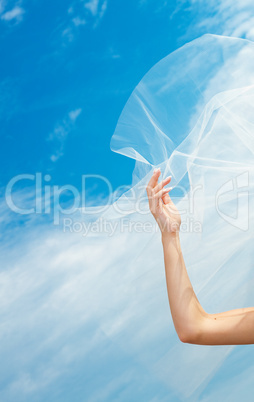 wedding dress and veil with a hand against the blue sky