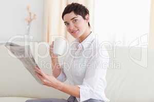 Woman with a cup reading the news while looking at the camera