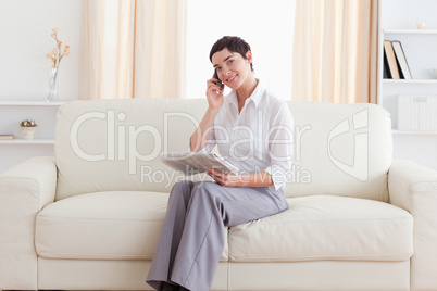 Beautiful Woman with a cellphone and a newspaper looking at the