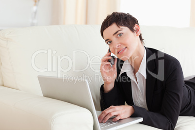 Cute Woman lying on a sofa with a laptop and a phone