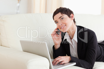 Charming Woman lying on a sofa with a laptop and a phone