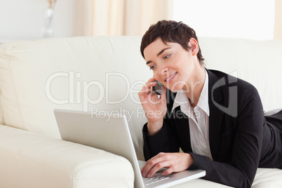 Smiling Woman lying on a sofa with a laptop and a phone