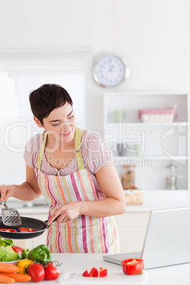 Smiling woman cooking with receipt on laptop