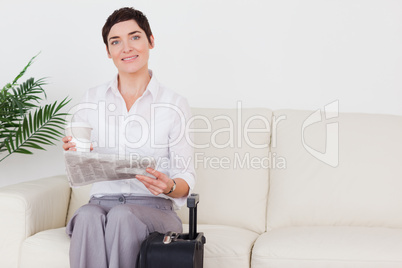 Short-haired smiling woman with a suitcase, a newspaper and a cu