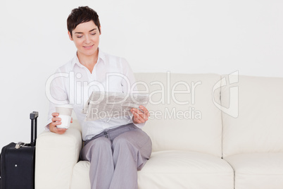 Happy woman with a suitcase, a newspaper and a cup