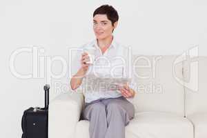 Happy brunette woman with a suitcase, a newspaper and a cup