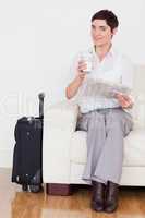 Brunette woman with a suitcase, a newspaper and a cup