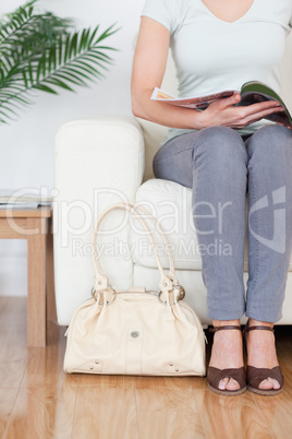 Part of a Woman on a sofa with a bag and a magazine