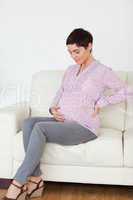 Pregnant woman sitting on a sofa touching her belly