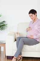 Smiling pregnant woman sitting on a sofa touching her belly