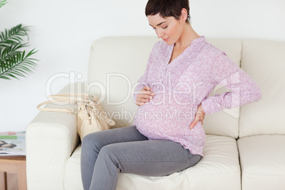 Charming pregnant woman sitting on a sofa touching her belly