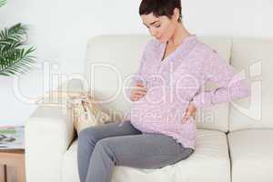 Charming pregnant woman sitting on a sofa touching her belly