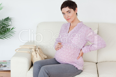 Gorgeous pregnant woman sitting on a sofa touching her belly
