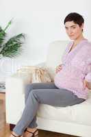 Brunette pregnant woman sitting on a sofa touching her belly