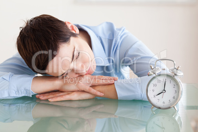 Sleeping woman with her head on the desk next to an alarmclock