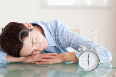 Sleeping businesswoman with her head on the desk next to an alar