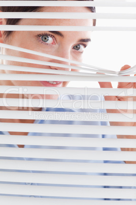 Beautiful brunette businesswoman peeking through a venetian blin