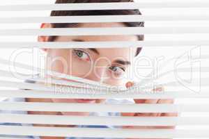 Cute businesswoman peeking through a venetian blind