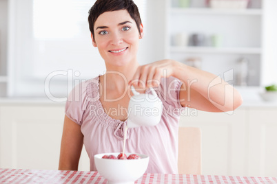 Woman pouring cream over strawberries looking into the camera
