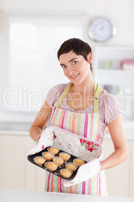 Smiling brunette woman showing muffins looking into the camera