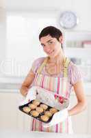 Smiling brunette woman showing muffins looking into the camera