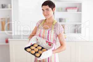 Charming brunette woman showing muffins looking into the camera