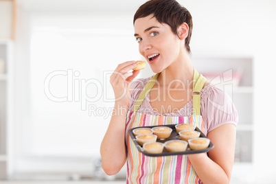 Joyful brunette woman showing muffins while eating one