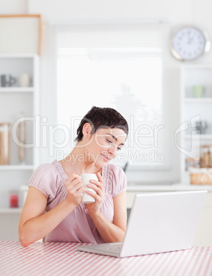 Smiling Woman holding a cup working with a laptop