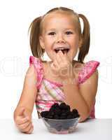 Cheerful little girl is eating blackberry