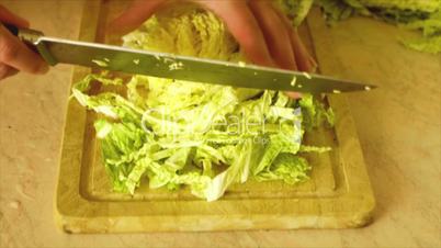 Woman cuts cabbage on wooden board in kitchen.
