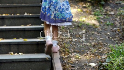 Little girl walks up stairs in summer city park.