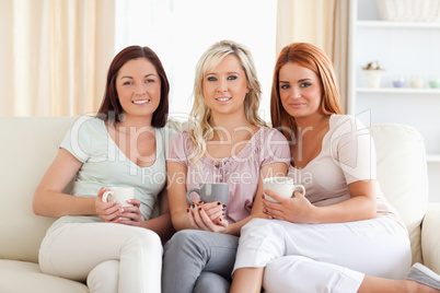 Charming women sitting on a sofa with cups