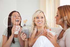Laughing women sitting on a sofa with cups