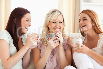 Joyful women sitting on a sofa with cups