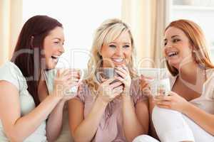 Joyful women sitting on a sofa with cups