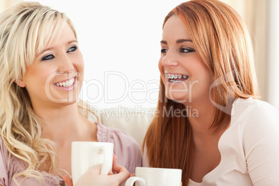 Laughing Young Women sitting on a sofa with cups