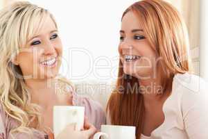 Laughing Young Women sitting on a sofa with cups