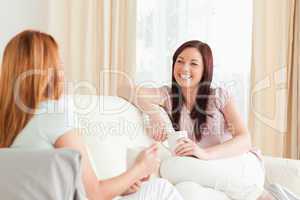 Charming young women sitting on a sofa with cups